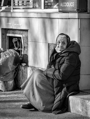 Bükreş, Romanya - 02.04.2022: Bükreş 'in merkezinde kaldırımda oturan yaşlı ve yalnız bir kadının portresi.