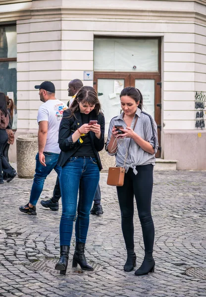 Bucharest, Romania - 04.08.2022: Two girls tourists in the Bucharest old town center searching for directions on their smartphones.