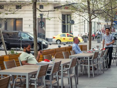 Bükreş, Romanya - 04.08.2022: Bükreş 'in merkezinde bir açık restoran ve kafede içki içen turistler ve yerel halk