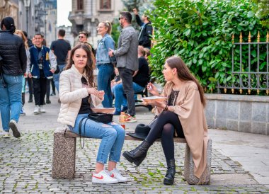 Bükreş, Romanya - 04.08.2022: Bükreş 'in eski şehir merkezinde bir bankta oturan iki güzel genç kız.