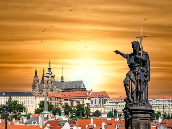 Statue of a saint on Charles Bridge pointing towards Prague Castel in Czech Republic. Beautiful sunset scene in Prague.