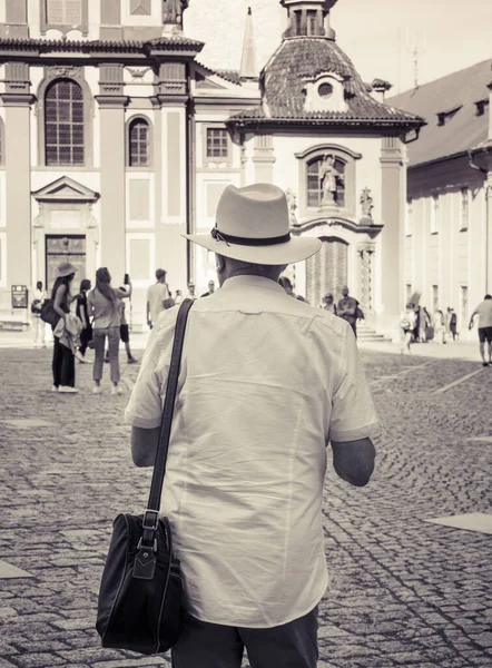 Black and white photography of a tourist man wearing a white hat. Rear view with a tourist in Prague Castle