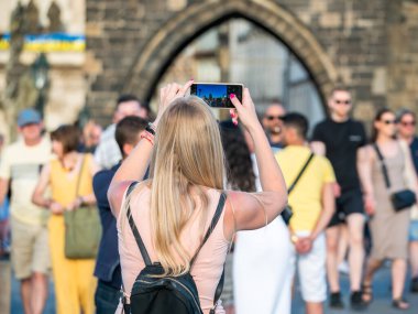 Charles Bridge, Prag 'da tanınmayan sarışın bir turist akıllı telefonuyla fotoğraf çekiyor.