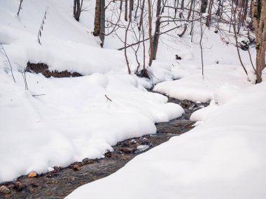 Beyaz donmuş karın altında akan bir dağ deresinin minimalist resmi..