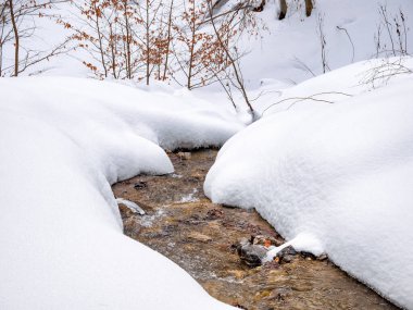 Beyaz donmuş karın altında akan bir dağ deresinin minimalist resmi..