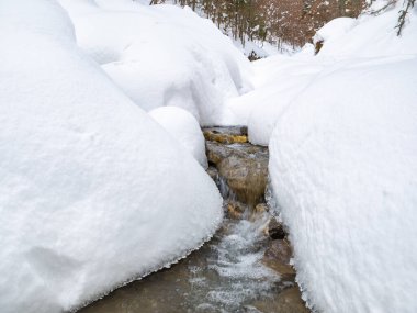 Beyaz donmuş karın altında akan bir dağ deresinin minimalist resmi..