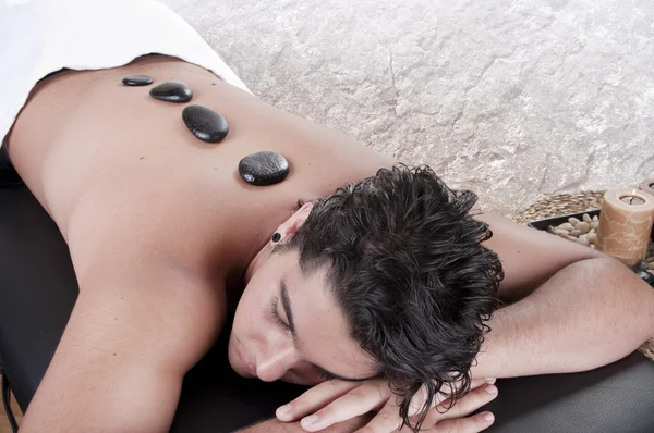 Мужчине делают массаж горячими камнями в спа-салоне — стоковое фото