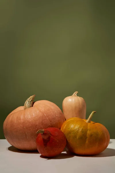 Quatre citrouilles sur table blanche contre mur vert. — Photo