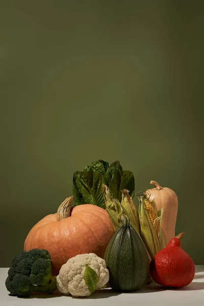 Säsongsgrönsaker på vitt bord mot grön vägg. — Stockfoto