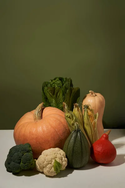 Säsongsgrönsaker på vitt bord mot grön vägg. — Stockfoto