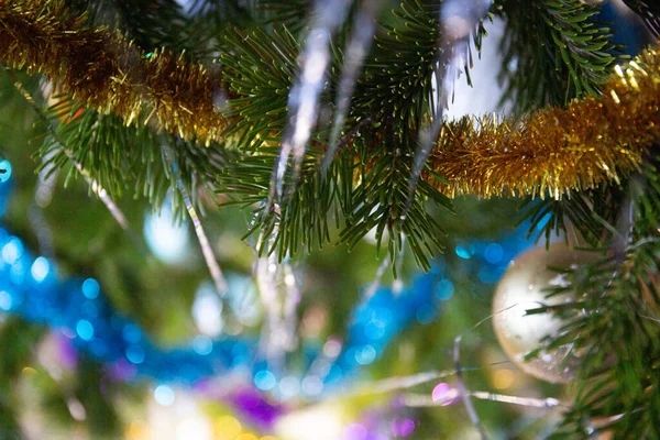 Decoraciones navideñas, oropel, destellos con un fondo borroso. El árbol de Año Nuevo en la víspera de Año Nuevo está iluminado con luces brillantes. Agujas de abeto de cerca. — Foto de Stock