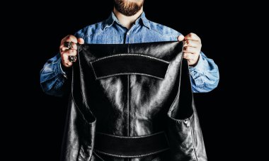 Motosikletli adamın resmi kot gömlekli, siyah arka planda yama renkleri olan deri bir yelek giyiyor..