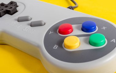 Sarı arka planda yatan klasik gri renkli 8 bitlik oyun konsolu denetleyicisinin yakın plan fotoğrafı.