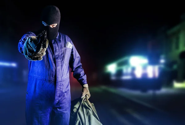 マスク バッグ 銃立ちフロントビューで強盗の写真や夜の通りの背景を目指して — ストック写真
