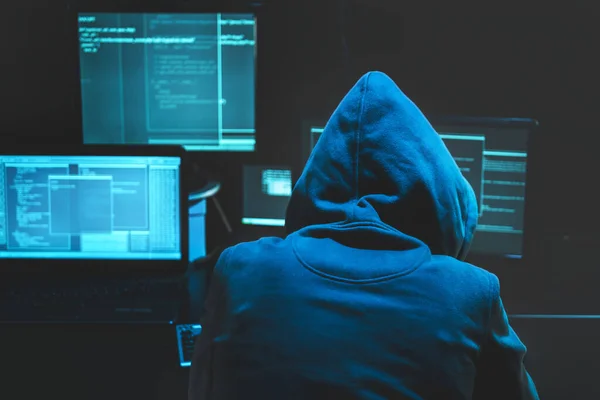 Hacker nutzen Computer, um massive Angriffe auf Regierungsserver zu organisieren. Hacker in Darkroom umzingelt Computer Stockbild