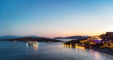 Lüks tatil köyü yakınlarındaki aydınlık tekneye gece görüşü. Renkli ışıklar su denizinin yüzeyini yansıtıyor. Avrupa turizm adalarındaki açık hava tatil beldesi. Geceleri liman manzarası. Resim indir