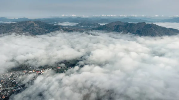 Bulutların üstünde. Karpatlar, Ukrayna 'da bir şehirle kaplı sisli bir dağ manzarası. Resim indir