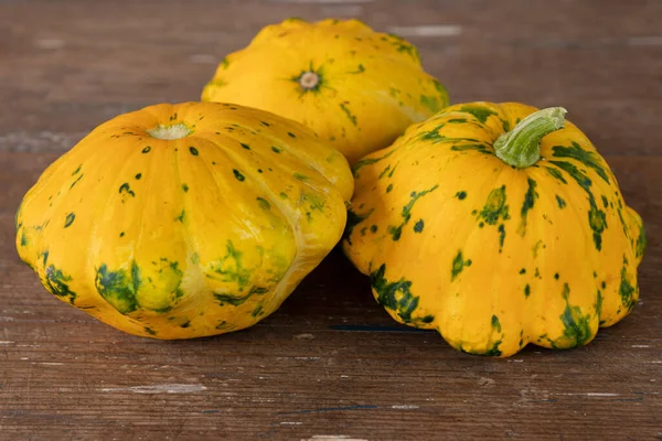 three patty pan squashes on wooden table, harvest of fresh vegetables, side view