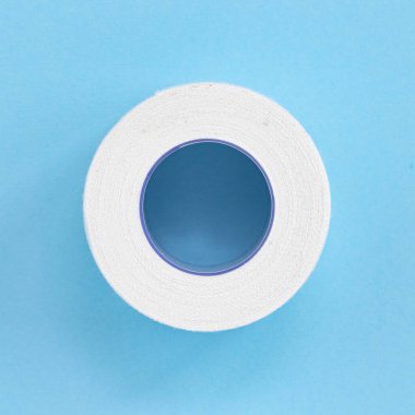 white roll band aid strip isolated on blue background, reel of adhesive bandage, top view