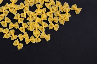 Siyah arkaplandaki yazı için boş alanı olan çiğ makarna farfalle, İtalyan mutfağının en üst görüntüsü.