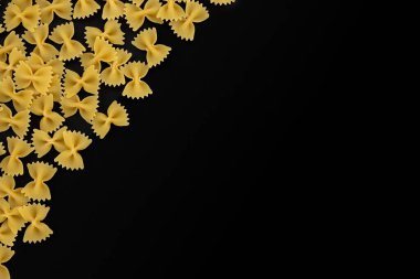 Siyah arkaplandaki yazı için boş alanı olan çiğ makarna farfalle, İtalyan mutfağının en üst görüntüsü.
