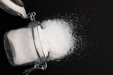 sea salt in glass jar isolated on black background, mineral product used in cooking and cosmetics, macro photo of seasoning, close up