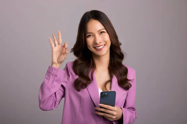 Cheerful Asian Woman Holding Smartphone Shows Sign Gray Background — 스톡 사진