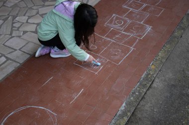 Küçük kız bahçede seksek oynuyor. Coronavirus karantinası sırasında açık havada renkli tebeşirlerle çizilen oyun..