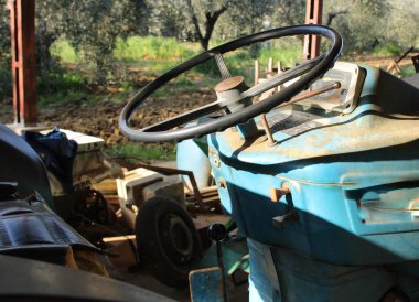 Eski mavi traktörün direksiyonu yakından görülebiliyor. Toskana tarlasının yetiştirilmiş zeytinliğinde. Direksiyon, kontrol paneli, vites kutusu, el freni ve ayarlanabilir koltuğu olan..