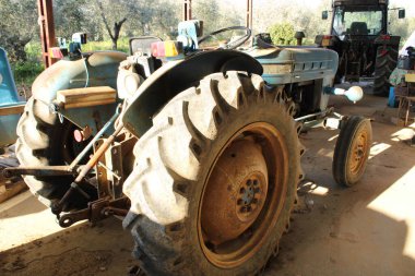 Eski mavi traktör, yeni traktör modelinin arkasındaki çiftlik kulübesine park edilmiş. Direksiyon, tekerlekler, ışıklar ve evrensel eklem ile römork bağlantısı.