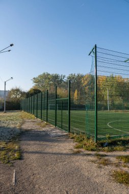 Etrafı yüksek çitlerle çevrili küçük bir okul stadyumu. Çitin arkasındaki High Shcool Futbol Stadyumu. Renkli bir sabah.