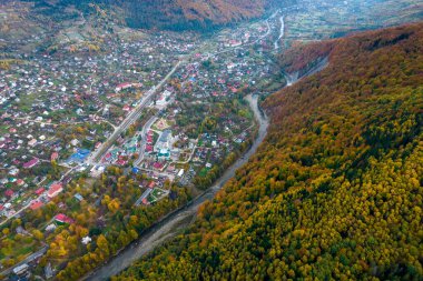 Sonbaharda dağlar arasındaki küçük köyün havadan aşağı manzarası. Sonbahar renklerine boyanmış dağların ve ağaçların peyzaj drone fotoğrafı
