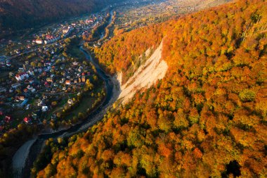 Sonbaharda dağlar arasındaki küçük köyün havadan aşağı manzarası. Sonbahar renklerine boyanmış dağların ve ağaçların peyzaj drone fotoğrafı