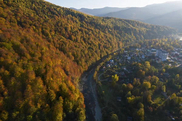 Sonbaharda dağlar arasındaki küçük köyün havadan aşağı manzarası. Sonbahar renklerine boyanmış dağların ve ağaçların peyzaj drone fotoğrafı