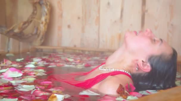 Krásná mladá žena ležící v horké ofuro lázni plné růžových květin. Květinová koupel s lístky růží. Mladá žena se koupe ve vaně plné okvětních lístků. Japonská lázeň