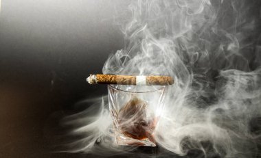 Siyah arka planda Küba Havana purosuyla viski içmek. Bir bardak viski ya da üzerinde sigara olan bir konyak..