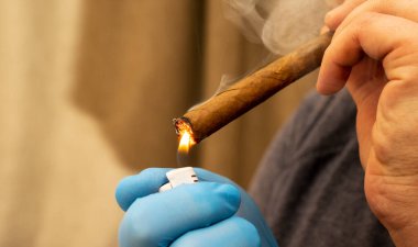 Bir iş adamının elindeki puronun yakın görüntüsü. Karanlık bir arka plan ışığı üzerinde erkek elleri yanan bir puro ve çakmak. Dumanlı arkaplan.