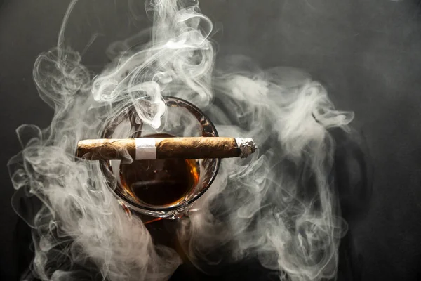 Siyah arka planda Küba Havana purosuyla viski içmek. Bir bardak viski ya da üzerinde sigara olan bir konyak..