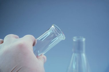 Mavi arka planda laboratuvar ekipmanlarını tutan bilim adamının yakın plan fotoğrafı.