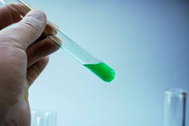 Mavi arka planda laboratuvar ekipmanlarını tutan bilim adamının yakın plan fotoğrafı.