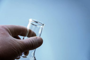 Mavi arka planda laboratuvar ekipmanlarını tutan bilim adamının yakın plan fotoğrafı.