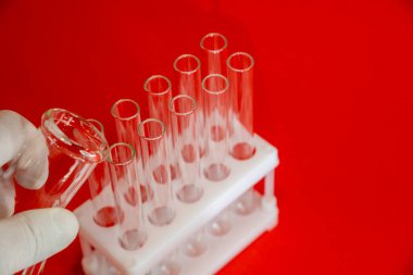 Kırmızı arka planda laboratuvar ekipmanlarını tutan bilim adamının yakın plan fotoğrafı.