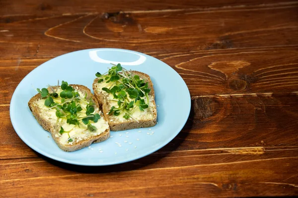 Kahvaltı için sandviç hazırla. Mavi tabakta mikro yeşillikli sandviçler ahşap arka planda lezzetli ve taze organik gıdalar sağlıklı kahvaltı konsepti