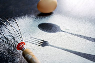 Üst kaşık ve çatal silueti koyu arkaplanda un ve yumurta ile yapılmış. Yumurta ve çırpılmış beyaz un. Kırsal zıtlık arka planı. Yemek hazırlama süreci. Fırın kavramı.
