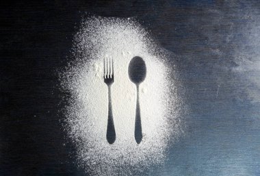 Üst kaşık ve çatal silueti koyu arkaplanda un ile yapılmış. Çatal ve kaşık silueti beyaz un üzerinde. Kırsal zıtlık arka planı. Yemek hazırlama süreci. Fırın kavramı.