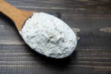 Whole flour in spoon on dark vintage wooden background. Close up view. Preparations for homemade baking. Basic ingredients for baking. Wheat flour on wooden spoon. 