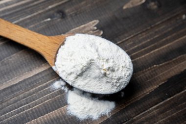 Whole flour in spoon on dark vintage wooden background. Close up view. Preparations for homemade baking. Basic ingredients for baking. Wheat flour on wooden spoon. 