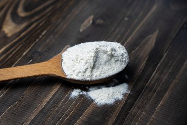 Whole flour in spoon on dark vintage wooden background. Close up view. Preparations for homemade baking. Basic ingredients for baking. Wheat flour on wooden spoon. 