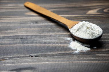 Whole flour in spoon on dark vintage wooden background. Close up view. Preparations for homemade baking. Basic ingredients for baking. Wheat flour on wooden spoon. 