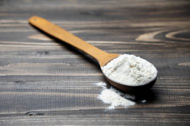 Koyu renkli ahşap arka planda kaşıkla un. Manzarayı kapat. Ev yapımı pişirme hazırlıkları. Pişirmek için temel malzemeler. Tahta kaşıkta buğday unu. 